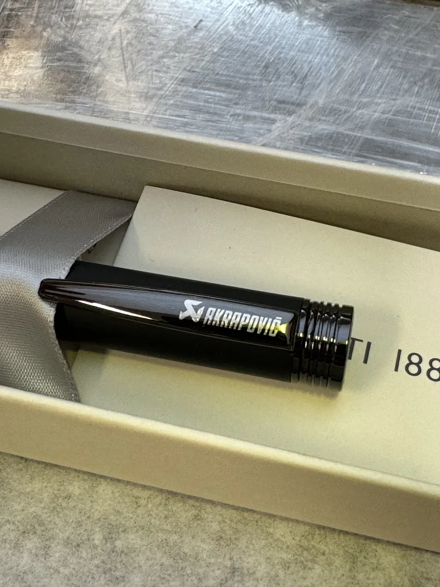 Black pen in a gift box with a white laser-engraved Akrapovič logo on the clip